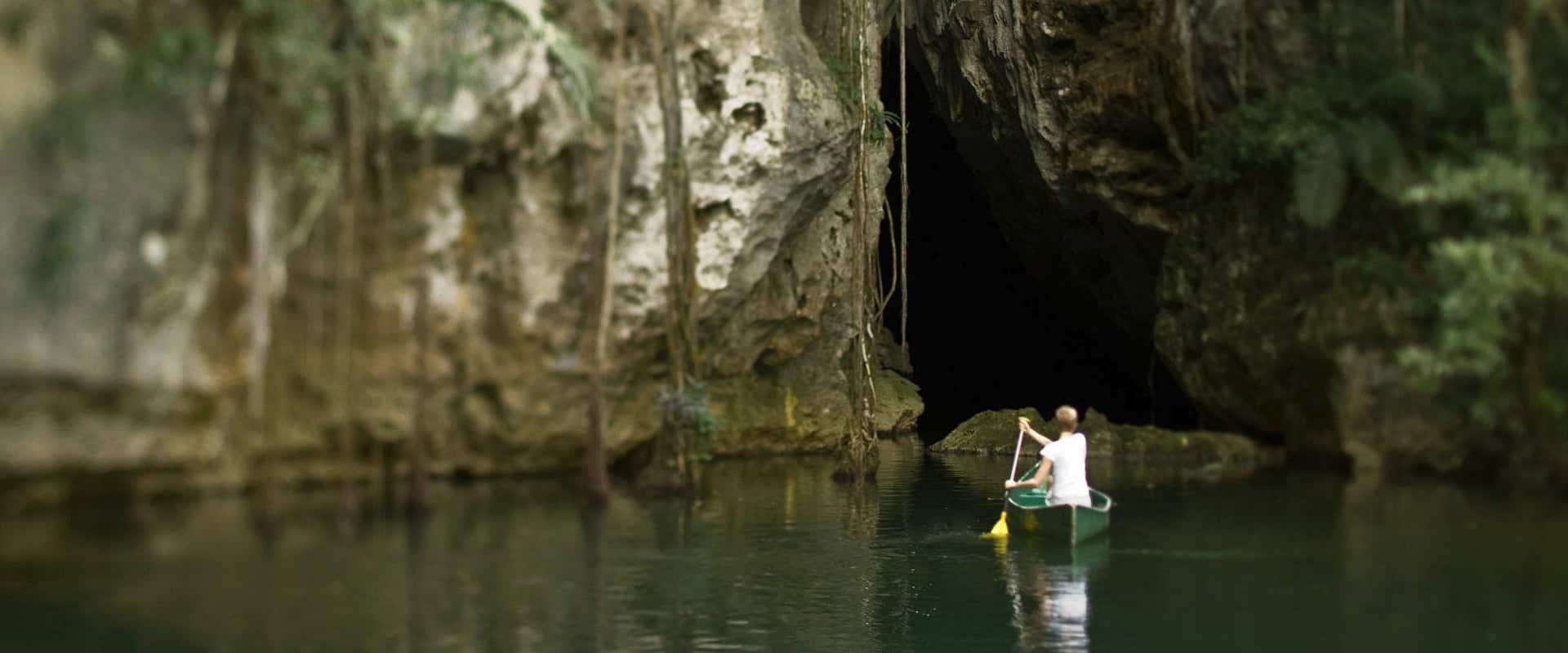 Exploring a dark cave entrance surrounded by lush greenery in Belize.